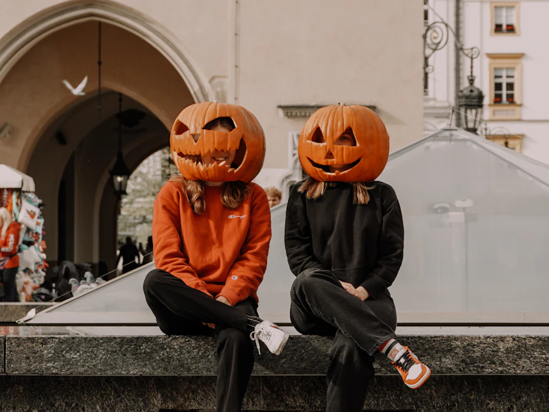 Two friends in pumpkin-head Halloween costumes sitting on a bench