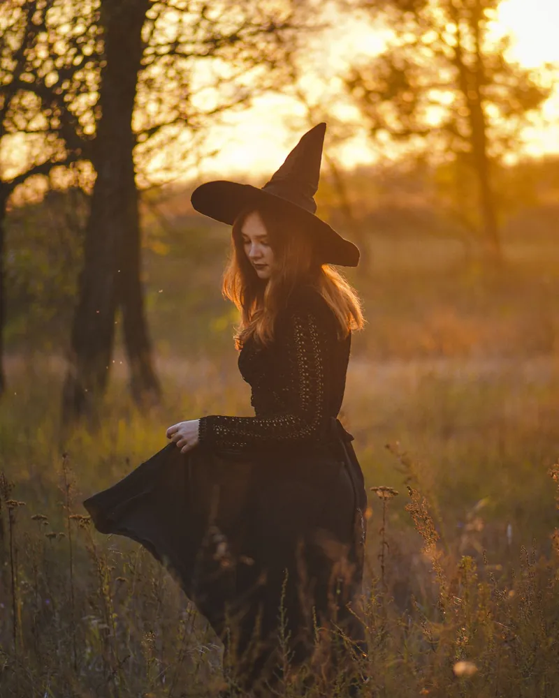 Woman in a witch costume walking through an autumn field at sunset