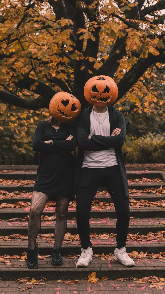 Couple wearing carved pumpkin heads on autumn steps