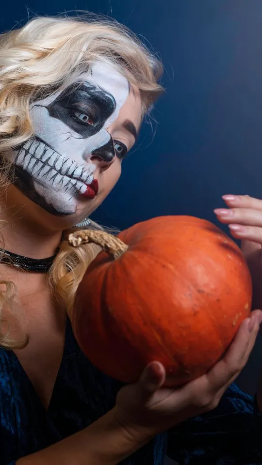 Woman with half-face skeleton makeup holding a pumpkin