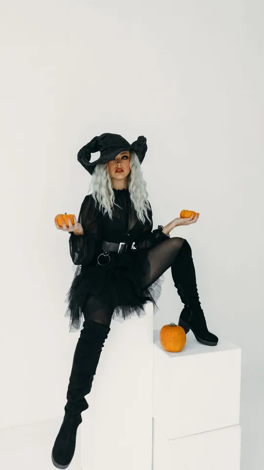 Woman in a black witch costume holding two small pumpkins